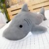 Une peluche de requin gris avec des yeux noirs et une bouche blanche sur un lit blanc.