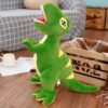 Un dinosaure en peluche vert avec des yeux noirs et une bouche ouverte, debout sur un sol en bois.