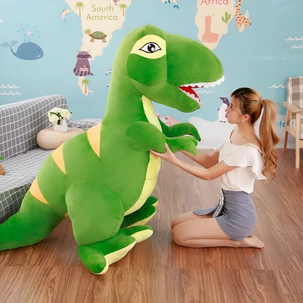 Une jeune femme souriante tenant un grand dinosaure vert en peluche. Le dinosaure est debout sur un plancher en bois. La pièce est décorée d'un papier peint à thème mondial.