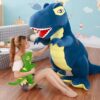 Une jeune femme assise sur un plancher en bois, tenant un dinosaure en peluche vert. Un grand dinosaure bleu en peluche se trouve à côté d'elle.