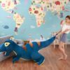 Une jeune fille joue avec un grand dinosaure en peluche bleu devant un mur avec une carte du monde.