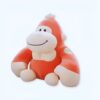 Une peluche de singe orange souriant assis sur un fond blanc.