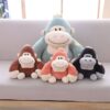 Quatre peluches de gorille souriants, un bleu, un brun, un orange et un noir, sur un canapé gris.