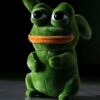 Une peluche verte en forme de grenouille avec une bouche orange et de grands yeux noirs.