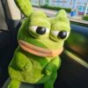 Une grenouille en peluche verte avec de grands yeux noirs et un visage triste assis dans une voiture.