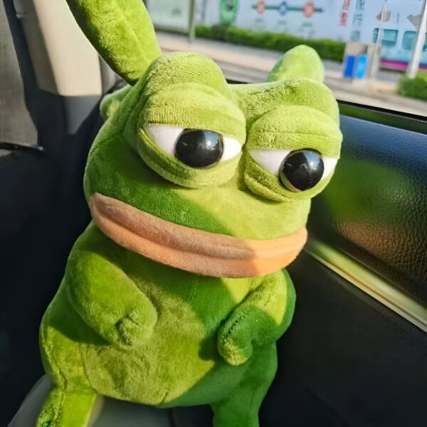 Une grenouille en peluche verte avec de grands yeux noirs et un visage triste assis dans une voiture.