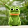 Peluche verte en forme de grenouille avec un grand sourire et des yeux noirs. La grenouille est assise sur un fond vert flou.