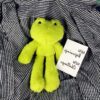 peluche-grenouille-verte-jouet-doux-pour-enfant-ideal-contre-la-peur-du-sommeil-2a-2 Une grenouille en peluche verte sur un tissu à carreaux noirs et blancs.