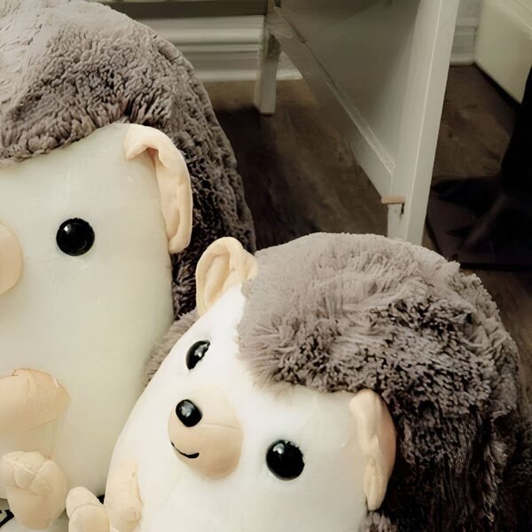 Deux hérissons en peluche, l'un blanc avec des yeux noirs et des piquants marrons, l'autre blanc avec des yeux noirs et des piquants marrons, posés sur un sol en bois.
