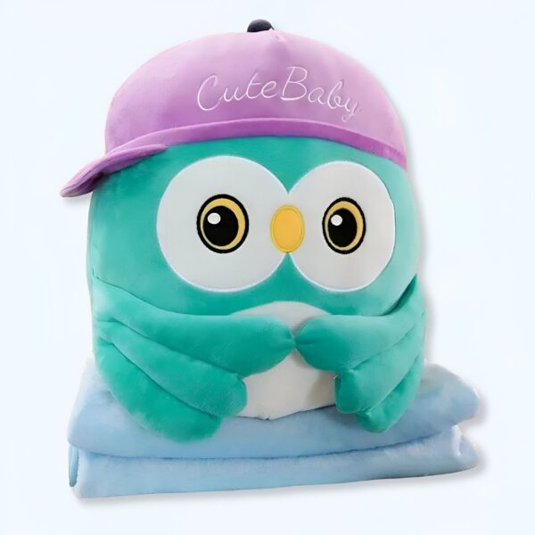 Une peluche hibou verte avec un chapeau violet portant l'inscription "Cute Baby" est posée sur une couverture bleue.