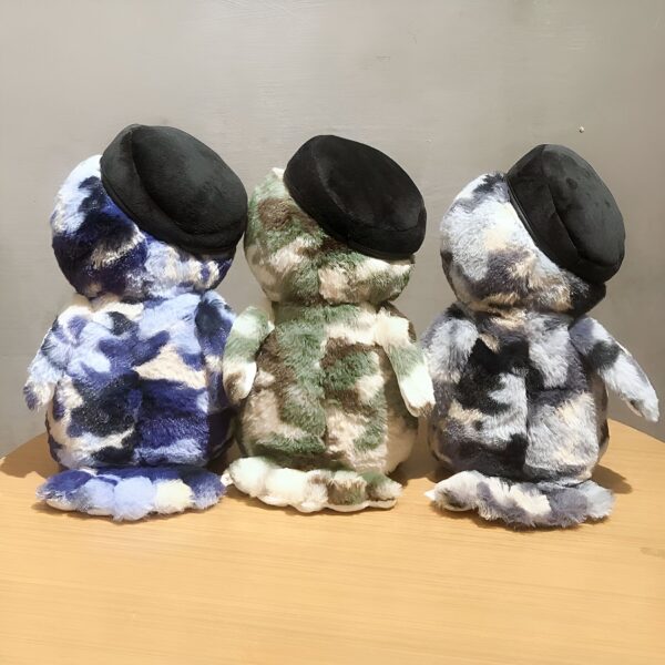 Trois peluches en forme de pingouin, portant des casquettes noires, sont alignées. Le pingouin de gauche est bleu, celui du milieu est vert et celui de droite est gris.