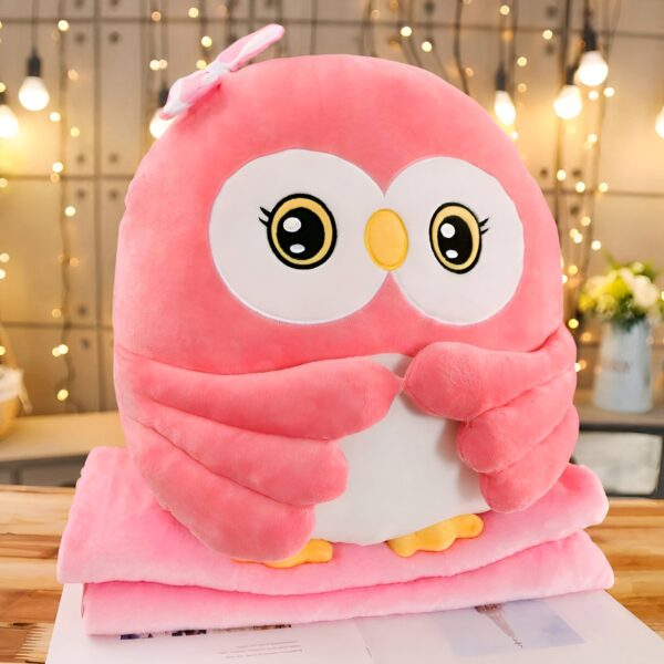 Peluche hibou rose avec un nœud sur la tête, assis sur une couverture rose.