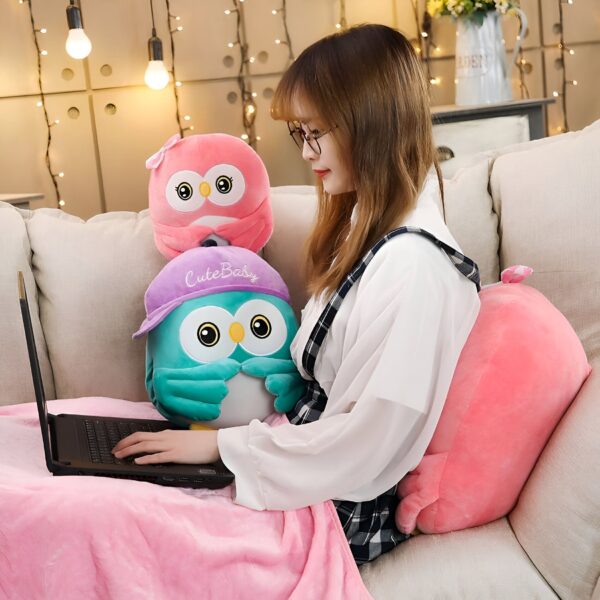 Une jeune femme assise sur un canapé avec un ordinateur portable sur ses genoux. Elle porte une robe blanche à carreaux noirs. Elle est entourée de trois peluches en forme de hibou.