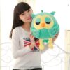 peluche-hibou-vert-yeux-fermes-doudou-hibou-pour-bebe-2a-3 Une jeune femme souriante tenant une peluche verte en forme de hibou.