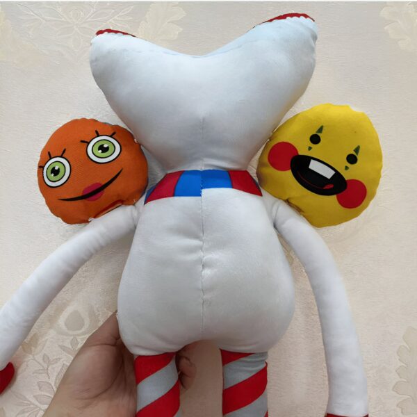 Peluche blanche avec deux têtes amovibles. La première tête est orange avec un sourire, la deuxième est jaune avec une seule dent.