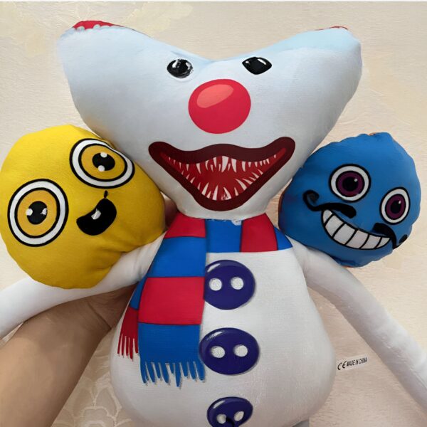 Une peluche blanche avec une écharpe rouge et bleue, un nez rouge, une bouche souriante avec des dents pointues, et des yeux noirs. Elle est entourée de deux autres peluches, une jaune avec des yeux jaunes et une bleue avec des yeux noirs, une moustache et une bouche souriante.