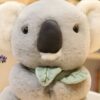 Un adorable koala en peluche gris avec des oreilles rondes, des yeux noirs et un noeud vert autour du cou.