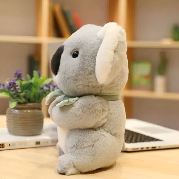 Une peluche de koala grise et blanche debout sur une table en bois, avec un fond flou.