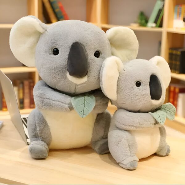 Deux adorables peluches koalas gris, l'un plus grand que l'autre, tenant chacun une feuille verte dans leurs pattes.