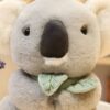 Une peluche de koala en fourrure grise avec un nœud vert en forme de feuilles.