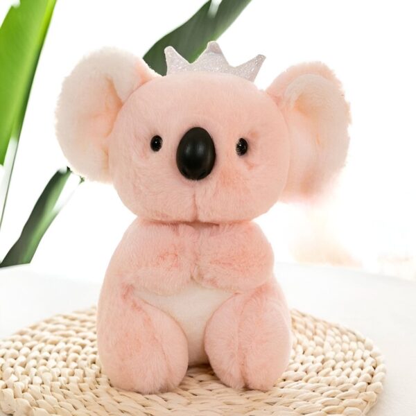 Une peluche rose en forme de koala portant une couronne. Elle est assise sur une surface en osier.