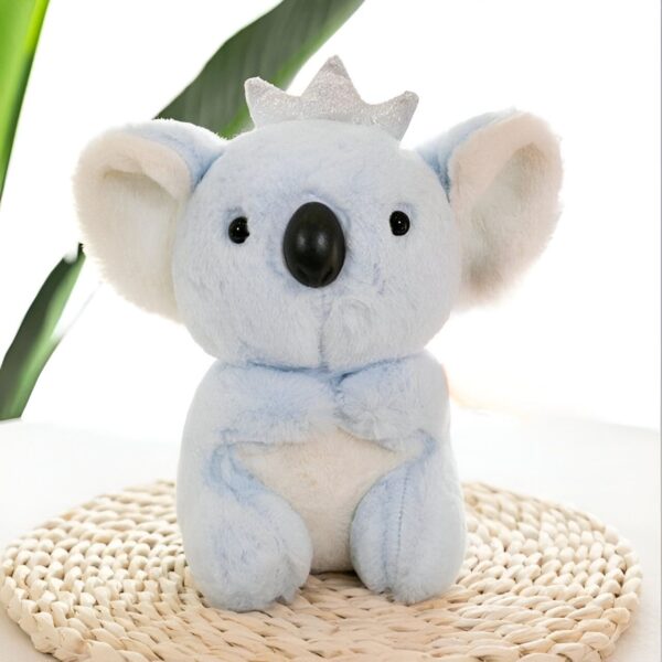 Peluche koala bleu portant une couronne, assis sur un tapis en osier.