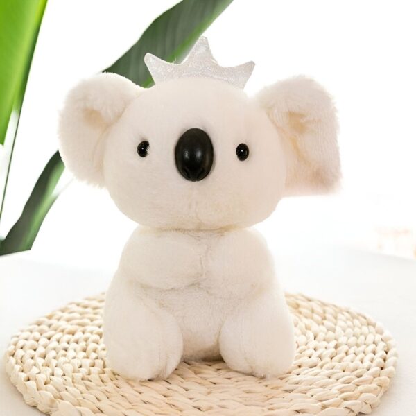 Une peluche blanche en forme de koala portant une couronne argentée, assise sur un tapis en osier.