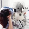 Une jeune femme allongée sur un lit avec un grand koala en peluche gris et blanc.