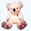 Gros ourson en peluche rose assis, avec des pattes roses et un nez noir. Il porte un nœud rose et un écusson avec un koala.