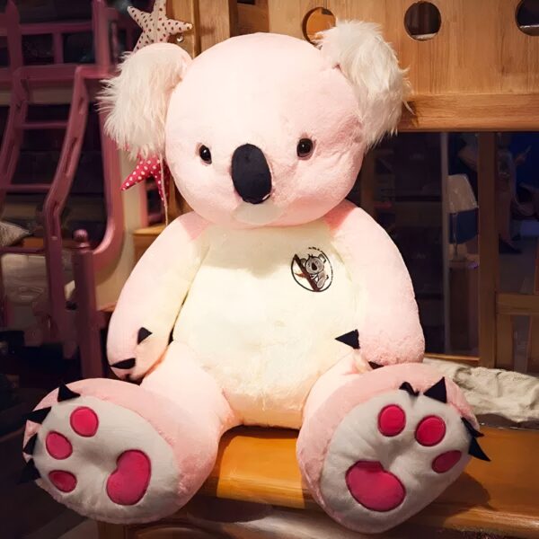 Grande peluche koala rose assis sur un banc en bois.