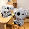 Trois peluches koala grises assises sur un bureau et une chaise, la plus grande tenant un jouet en forme de tronc d'arbre.