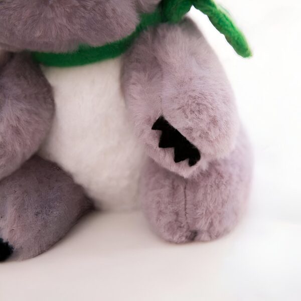 Peluche gris avec des détails noirs et un ruban vert.