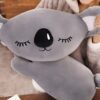 peluche-koala-grise-oreiller-doux-pour-dormir-3a Un coussin en peluche gris en forme de koala avec des yeux fermés et un nez noir.
