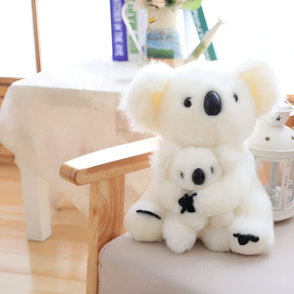 Deux peluches de koala blancs, l'un tenant l'autre, assis sur un fauteuil en bois clair.