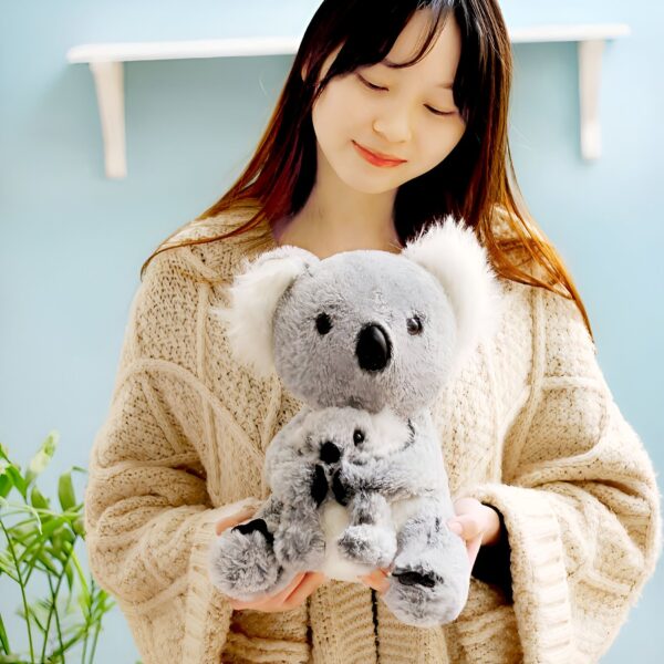 Une jeune femme en chandail beige tient une peluche de koala grise et blanche.