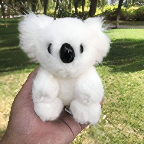 Une peluche blanche de koala dans une main avec un fond vert.