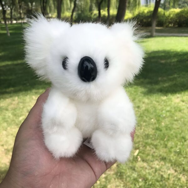 Une peluche blanche de koala avec de grands yeux noirs et un nez noir, tenue dans une main.