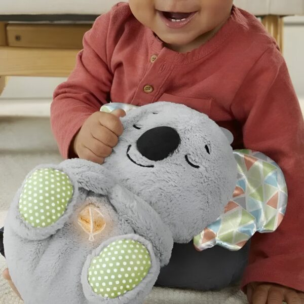 Un bébé souriant tient une peluche koala grise avec des détails multicolores et des points verts.