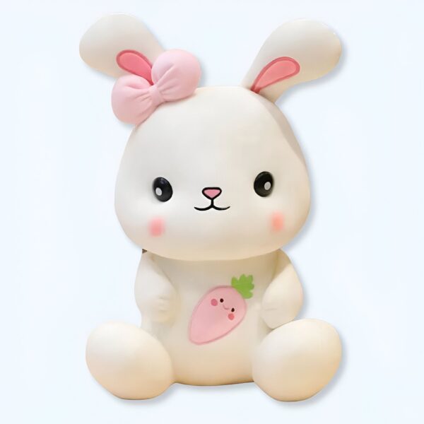 Un lapin en peluche blanc avec un nœud rose et une carotte brodée sur le ventre.