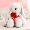 Un lapin en peluche blanc tenant une rose rouge sur un lit blanc.