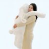 Une femme souriante tenant un gros lapin en peluche blanc.