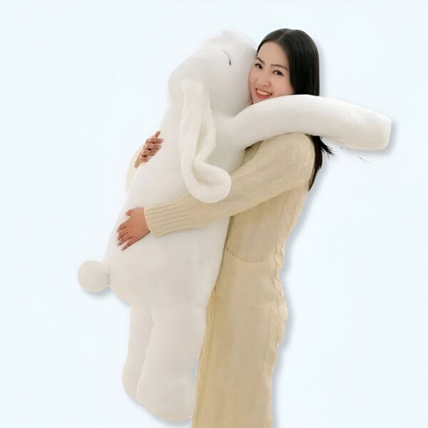 Une femme souriante tenant un gros lapin en peluche blanc.