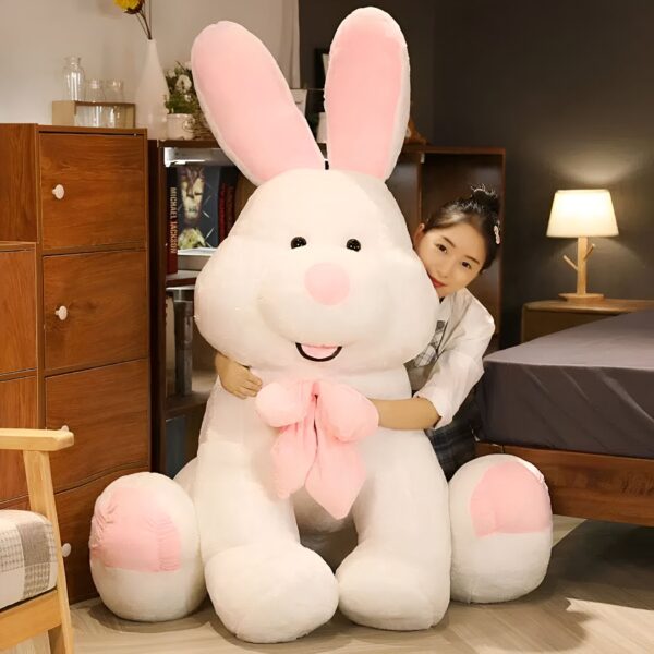 Une jeune femme étreint un gros lapin en peluche blanc avec un nœud rose.