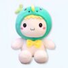 Peluche de bébé souriant avec un chapeau vert en forme de dinosaure et un noeud jaune.