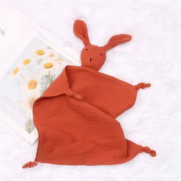 peluche-lapin-doudou-bebe-en-coton-et-mousseline-3a-3 Une couverture en tissu doux de couleur rouille avec une tête de lapin brodée. La couverture est parfaite pour les bébés et les jeunes enfants.