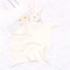 peluche-lapin-doudou-bebe-en-coton-et-mousseline-4a-2 Une couverture blanche en mousseline avec un lapin blanc en peluche attaché. La couverture est posée sur une surface blanche.