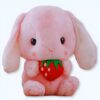 Un lapin rose en peluche tenant une fraise rouge.