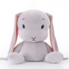 Gros lapin en peluche gris avec de longues oreilles roses assis sur un fond blanc.