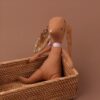 Un lapin en tissu brun avec des oreilles à fleurs jaunes et un nœud rose dans un panier en osier.