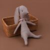 Un lapin en tissu gris avec un nœud rose est assis sur un panier en osier.